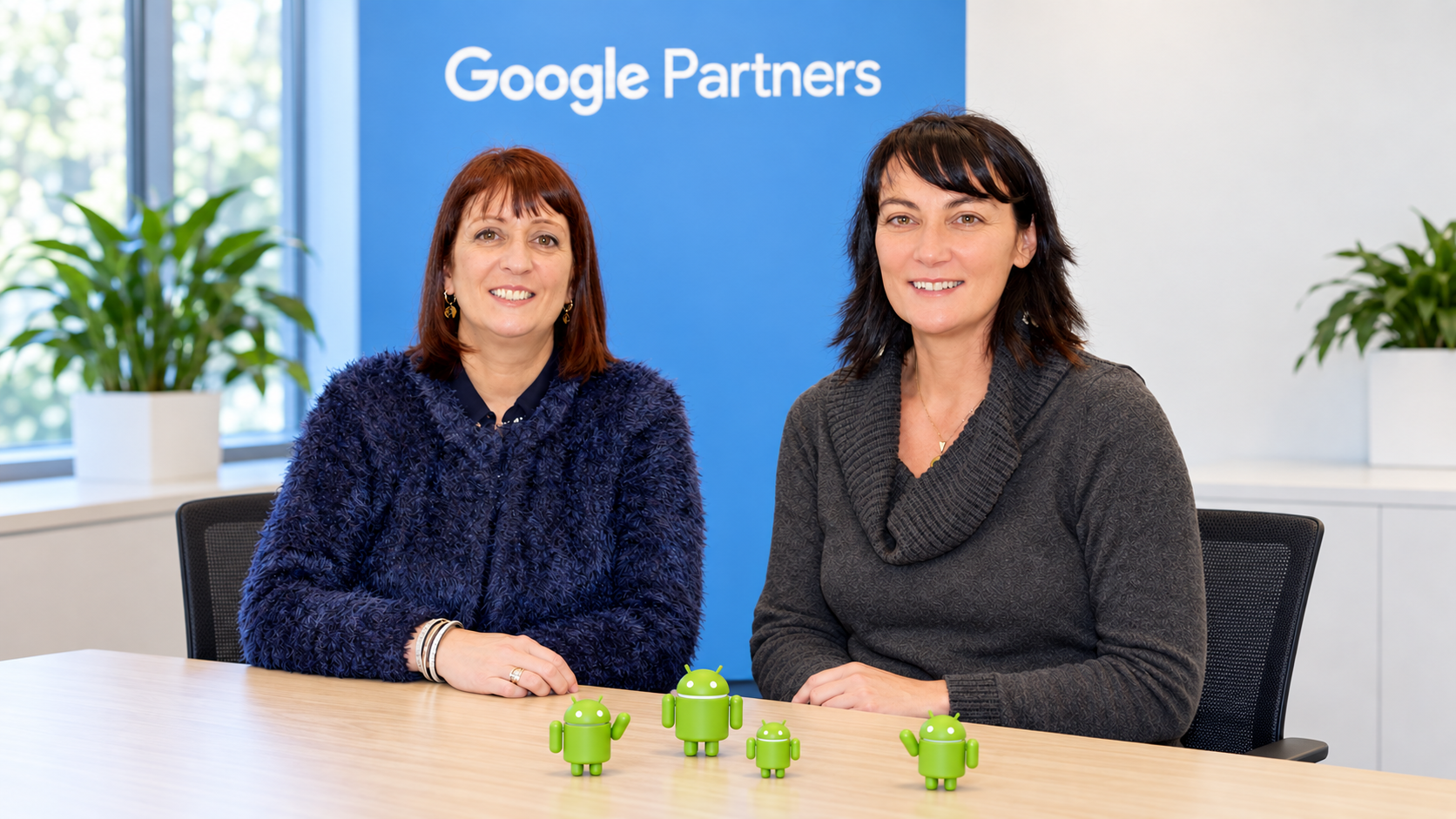 Karine Kugler seated at a Google Partners event table with a representative, with a Google Partners banner and Android collectibles on the table